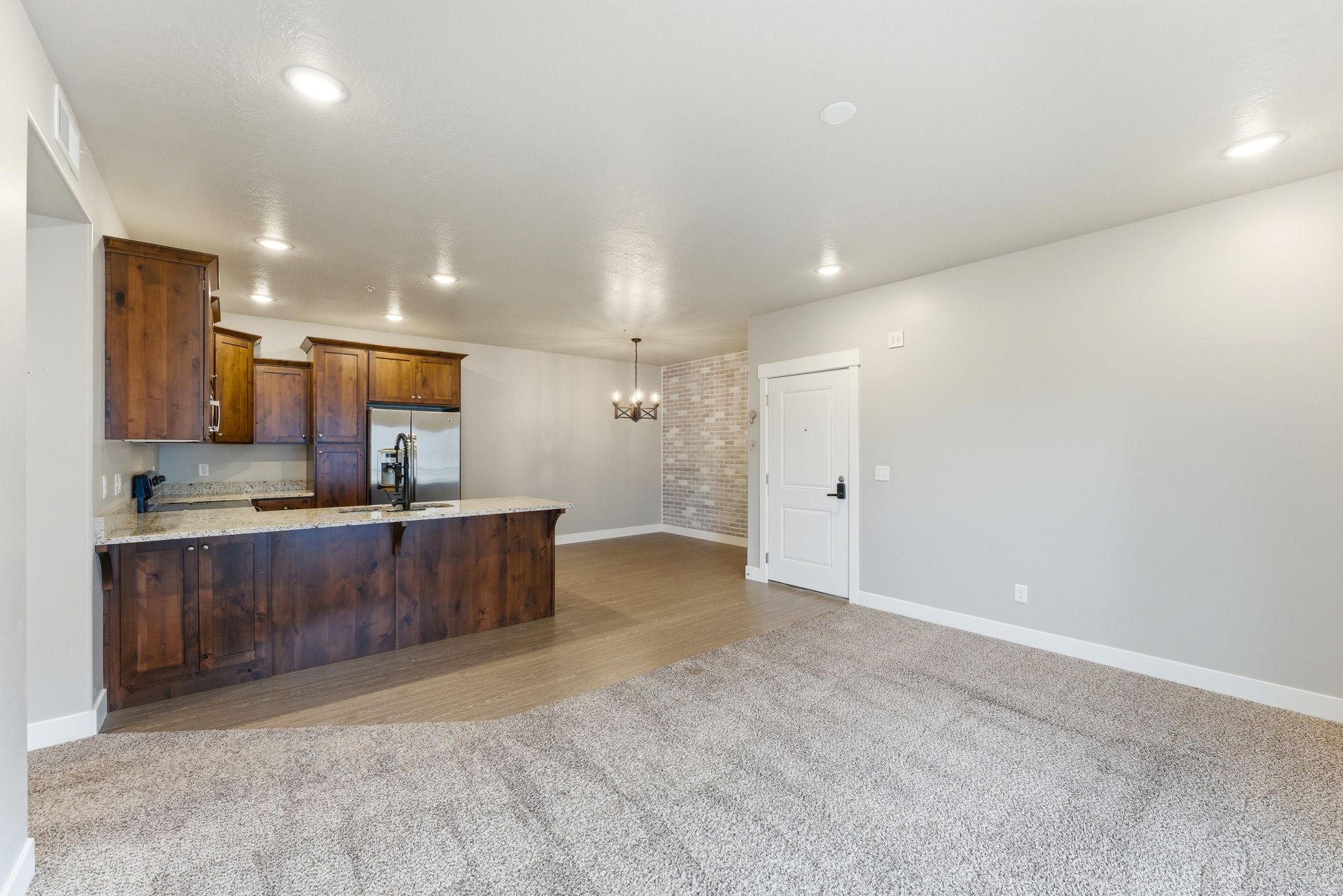 Open concept living space featuring a carpeted area, wood-finish flooring, and a kitchen with wood cabinetry, light-colored countertops, and stainless steel appliances
