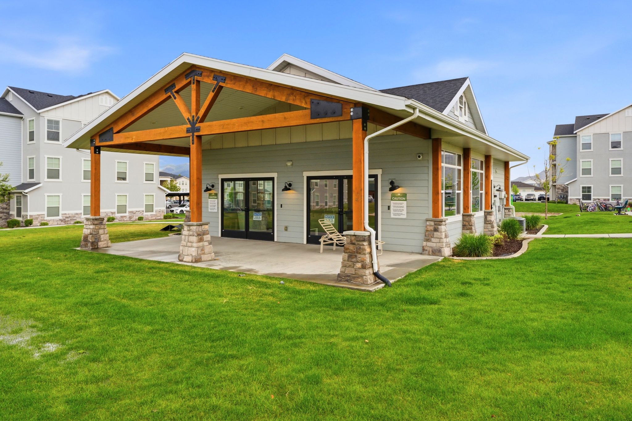 Craftsman-style clubhouse featuring a covered patio, exposed wood beams, stone column bases, and expansive glass doors