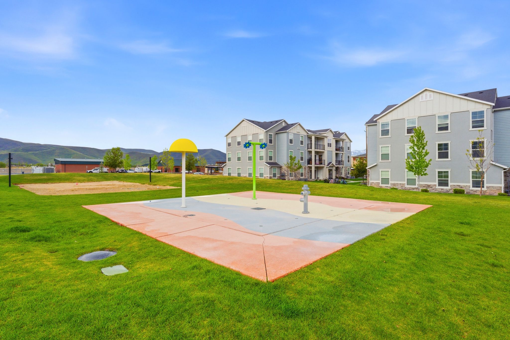 Recreational splash pad with colorful surfacing, surrounded by manicured green space