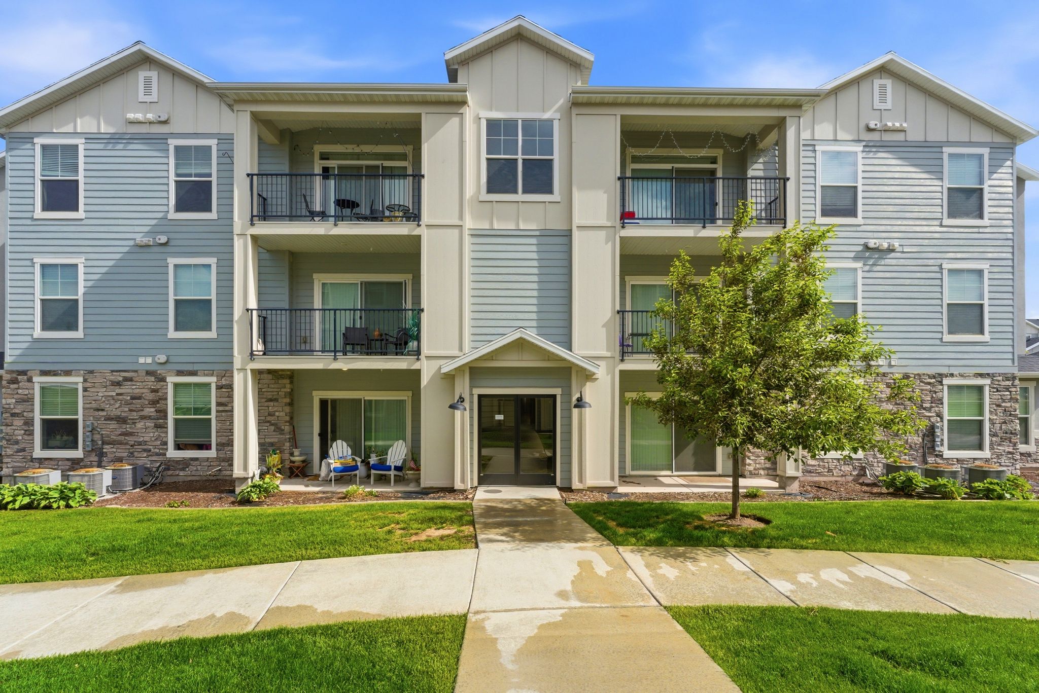 Contemporary multi-story building featuring light blue horizontal siding, stone veneer accents, and white trim