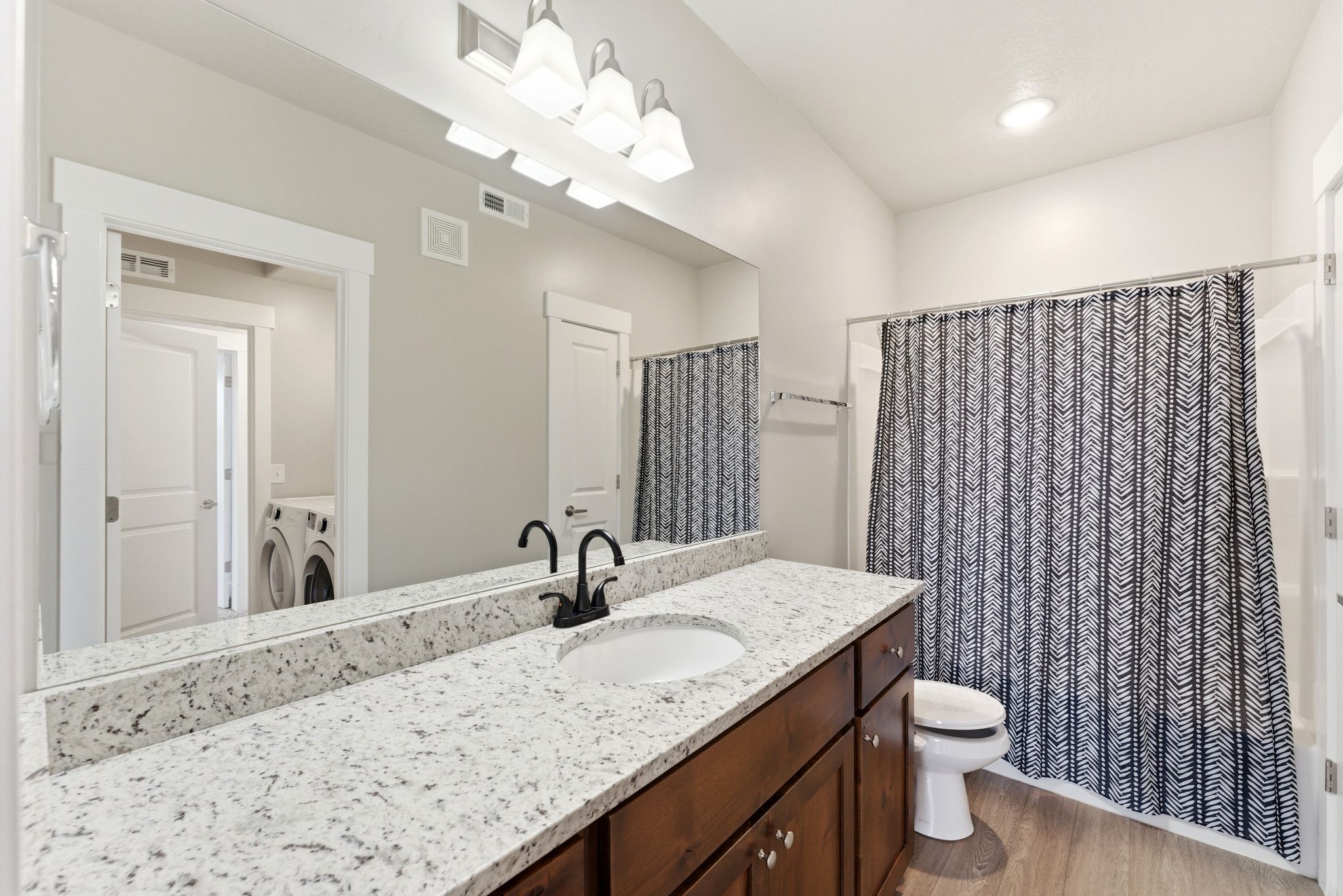 Bathroom featuring a dark wood-finish vanity with an undermount sink, a light granite countertop, and matte black fixtures