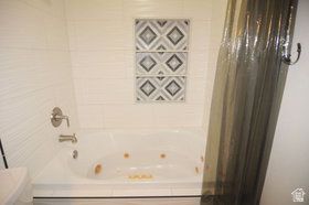 Bathroom featuring a jetted tub, white tile surround, brushed nickel fixtures, and decorative accent tiles
