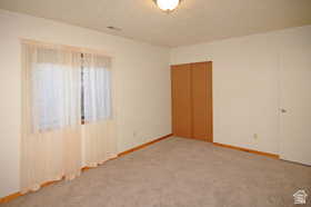 Carpeted room featuring a window with sheer drapes, bi-fold closet doors, a white door with a round knob, wood baseboards, and a ceiling-mounted light fixture