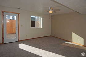 Spacious room featuring neutral wall tones, gray carpeting, a multi-speed ceiling fan with integrated lighting, and a glass-paneled door providing outdoor access