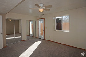 Carpeted interior space featuring a ceiling fan with integrated lighting, two sets of mirrored closet doors, a single-pane window, and a glass-paneled exterior door