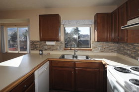 Kitchen featuring wood cabinetry, stone-look tile backsplash, and a double basin stainless steel sink