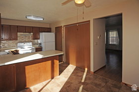 Kitchen featuring wood-finish cabinetry, white appliances, a tile backsplash, and a breakfast bar with a light-colored countertop