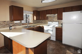 Kitchen featuring wood-finish cabinetry, light-toned countertops, a textured tile backsplash, and a window above the sink