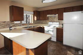 Kitchen featuring wood-finish cabinetry, light-toned countertops, a textured tile backsplash, and a window above the sink
