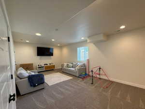 Spacious family room featuring neutral carpeting, recessed ceiling lighting, a wall-mounted television, and a window with blinds