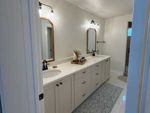 Primary ensuite dual vanity with light cabinetry and stone-finish countertops