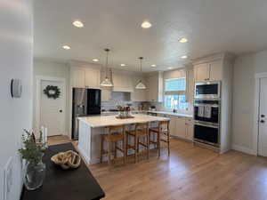 Open-concept kitchen featuring an oversized island with seating, pendant lighting, recessed ceiling lights, stainless steel appliances, and wood-finish flooring