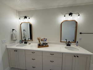 Primary ensuite dual vanity featuring white shaker-style cabinetry, white countertops, and black hardware