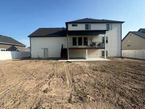 Rear exterior featuring a second-story deck with black metal railings, a ground-level concrete patio, and a spacious undeveloped yard