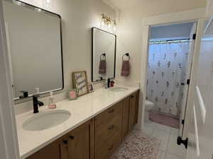Guest bathroom with double vanity featuring wood-finish cabinetry, white countertops, and matte black fixtures