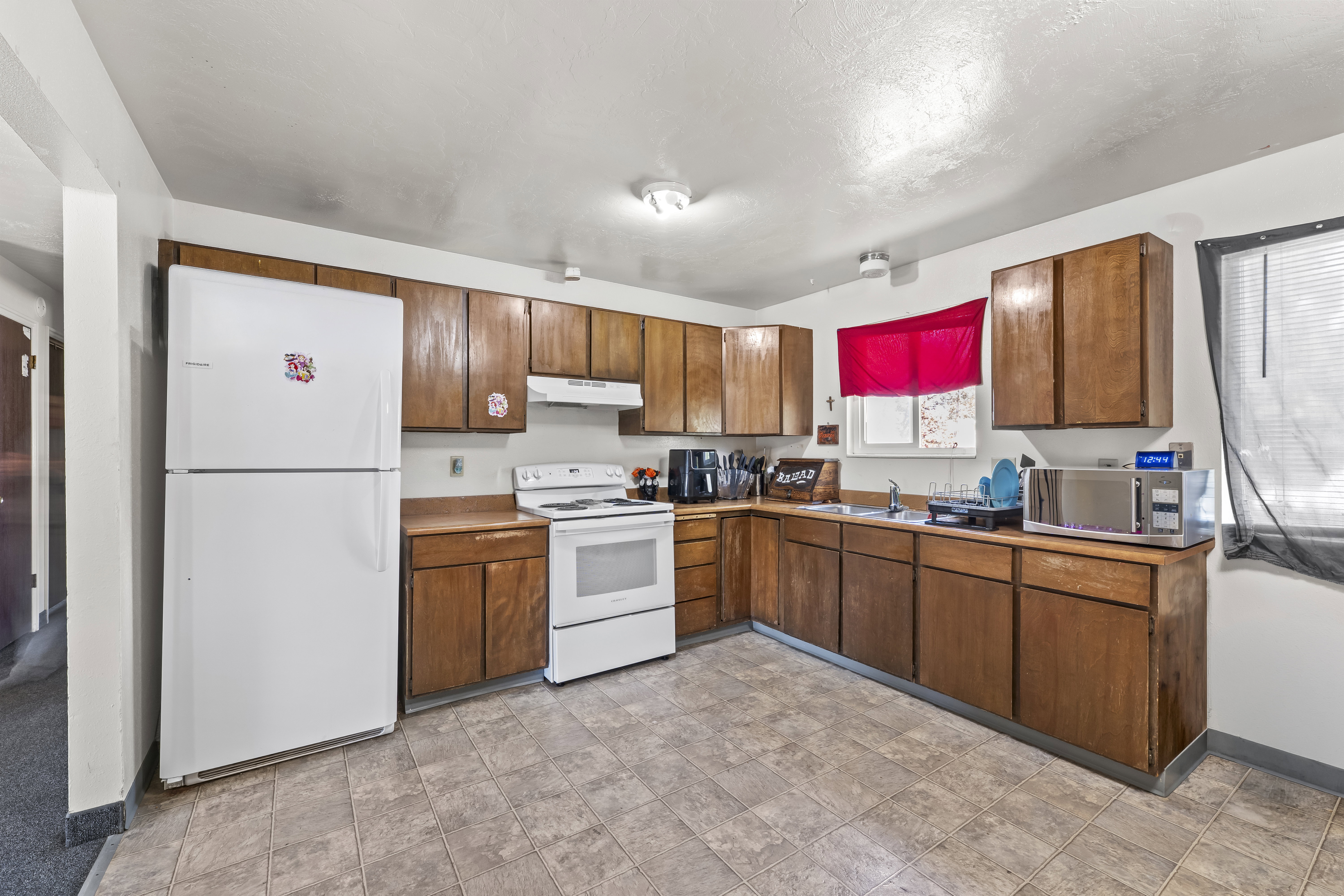 Kitchen featuring L-shaped wood-finish cabinetry and countertops, white appliances, and resilient flooring