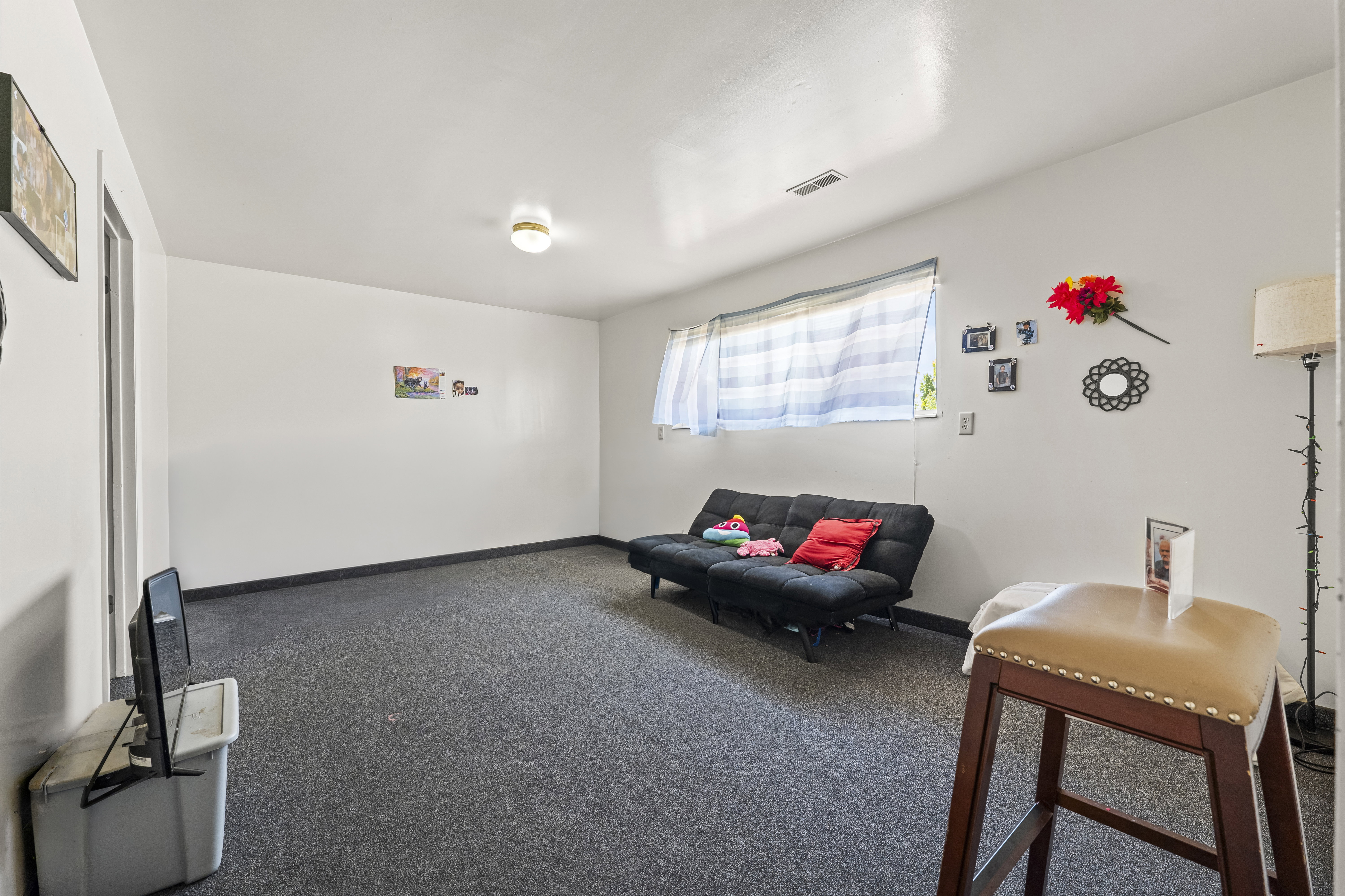 Spacious room featuring neutral white walls, a single window with blinds, and dark gray carpeting