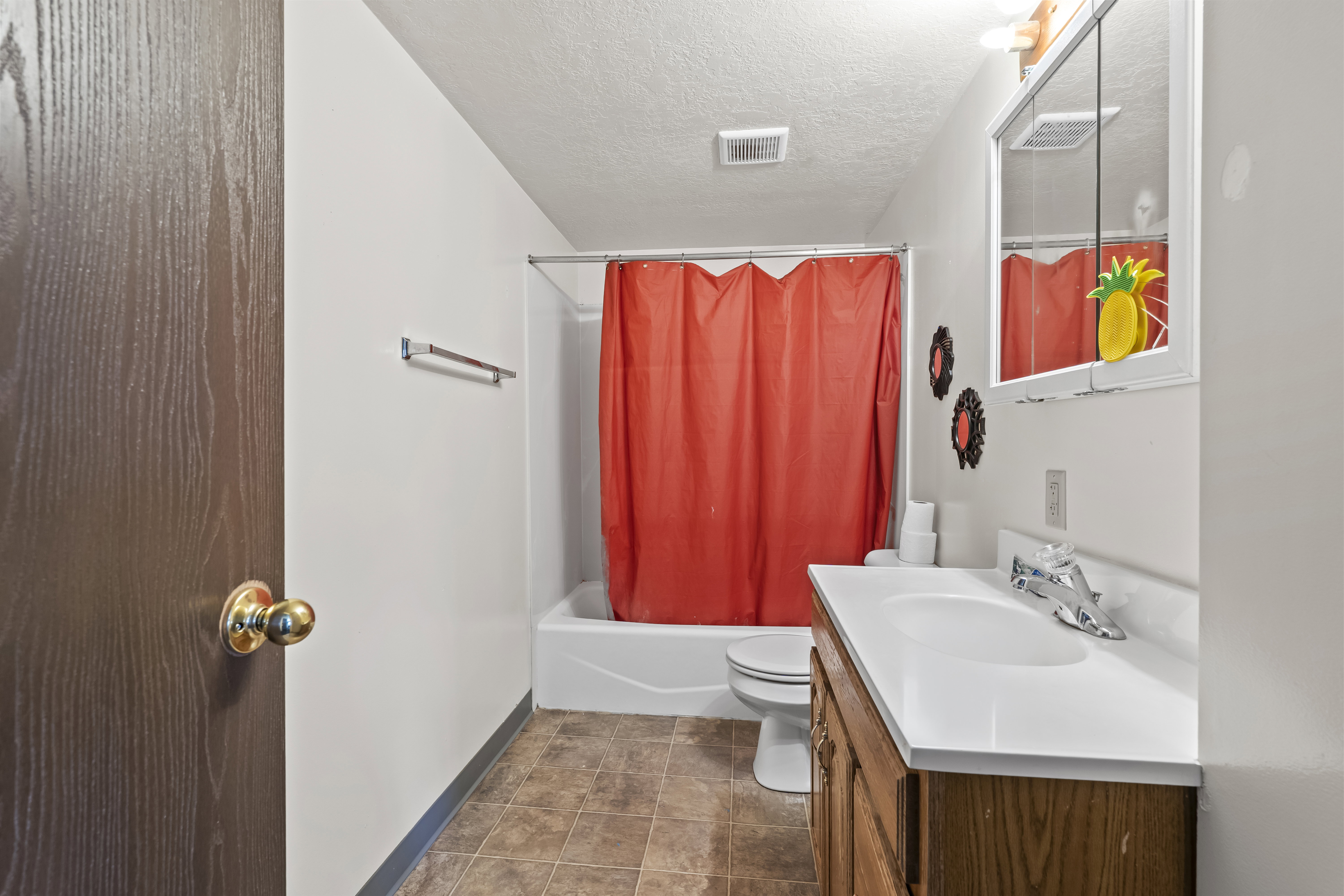 Bathroom featuring a wood-finish vanity with an integrated sink and chrome faucet, a medicine cabinet, and a white bathtub with a shower kit