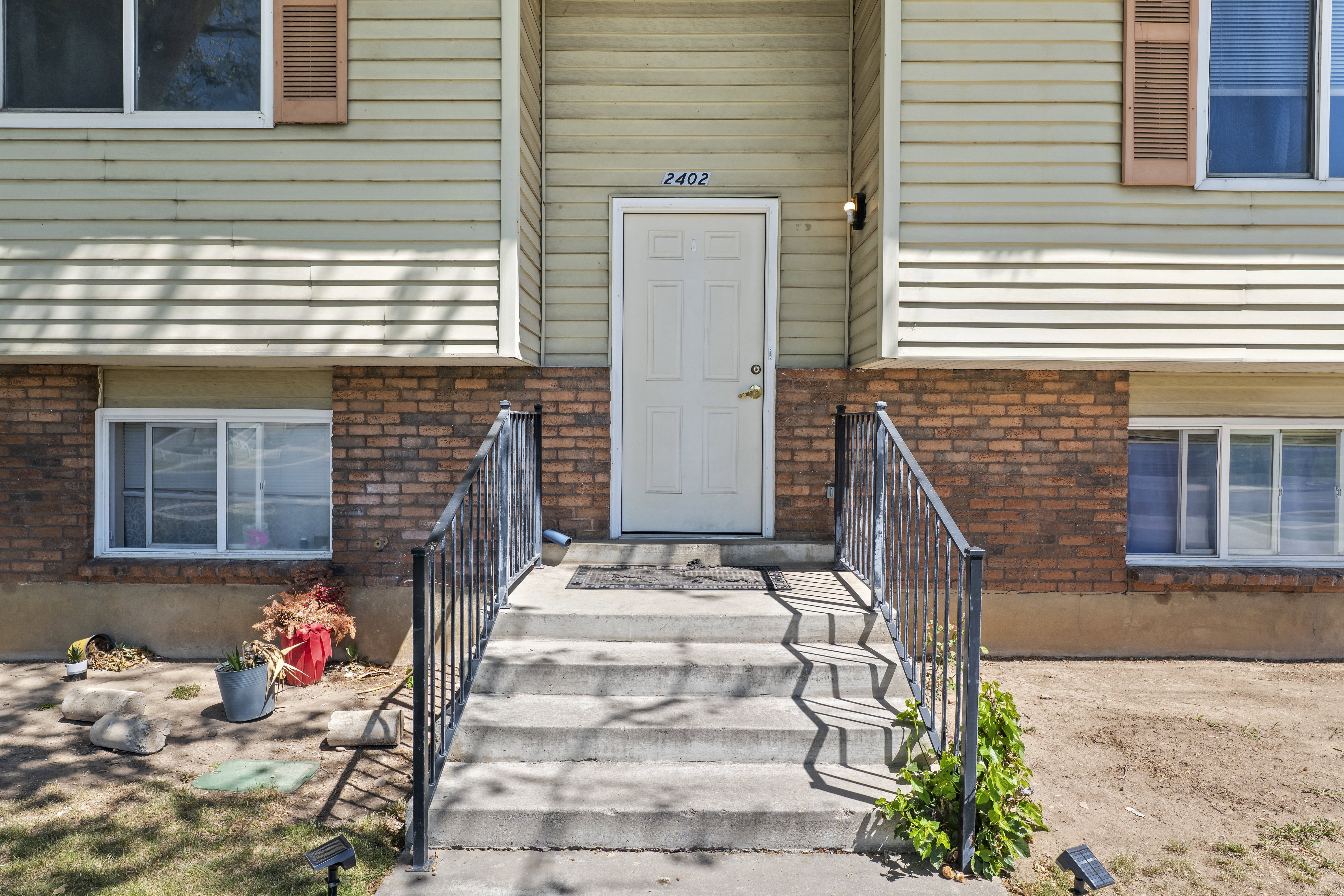 Front entry featuring concrete steps with wrought iron railings, a light-colored main door, and exterior siding with brick accenting