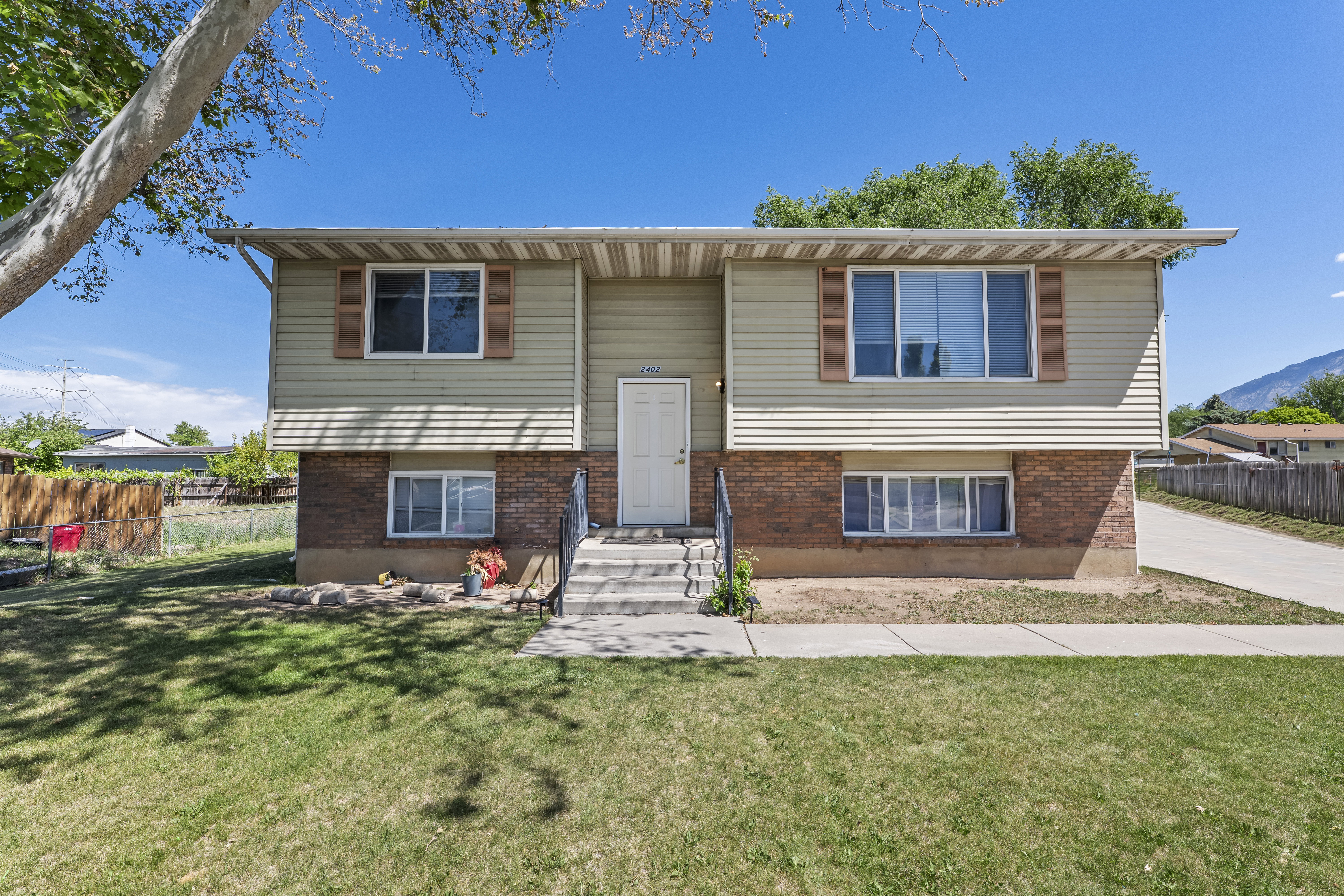 Split-level residence featuring a brick and siding exterior, front yard with mature tree, and concrete walkway