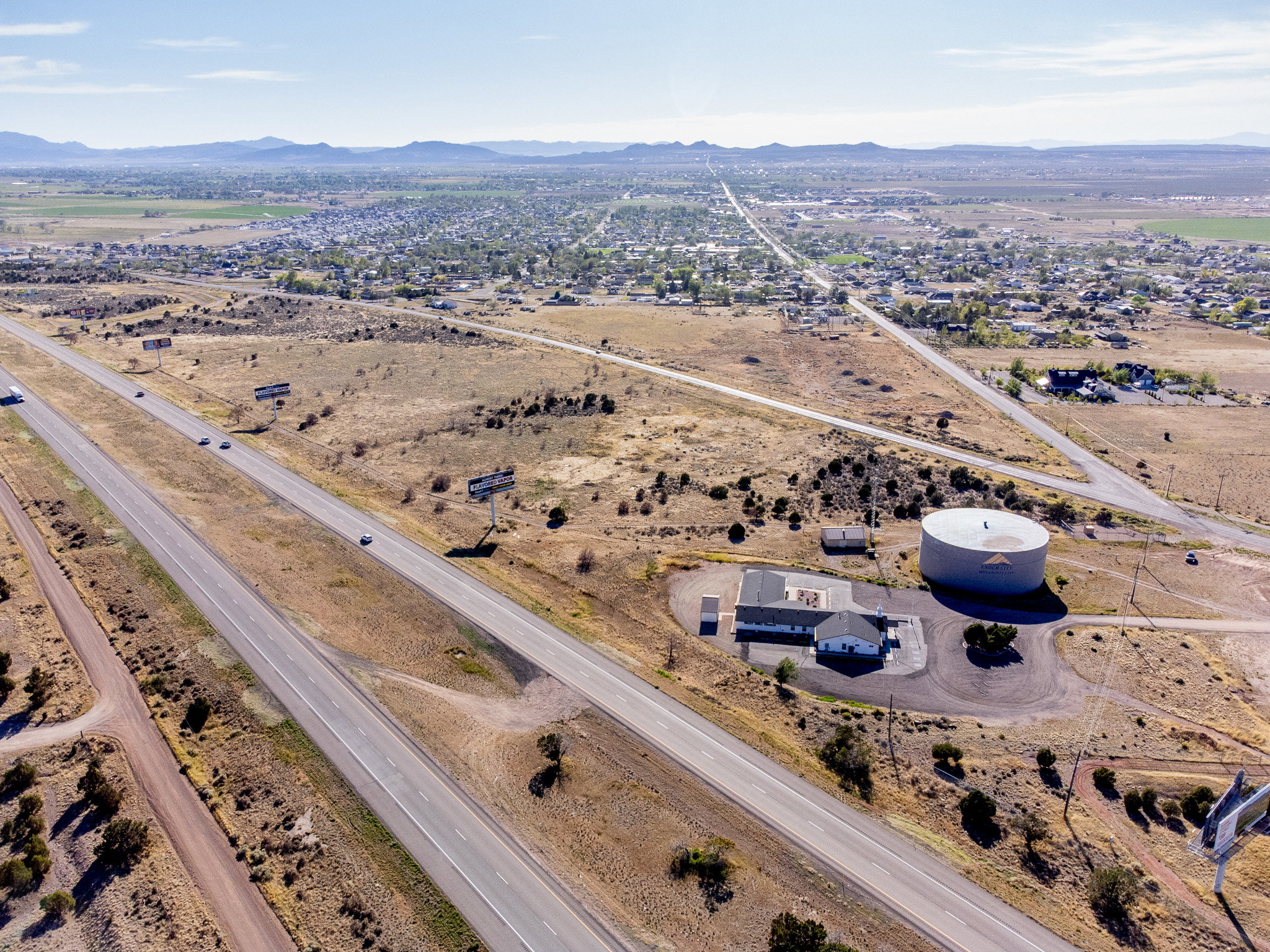 Expansive land parcel featuring highway frontage, a commercial building with a gray roof, a large water storage tank, and surrounding undeveloped terrain