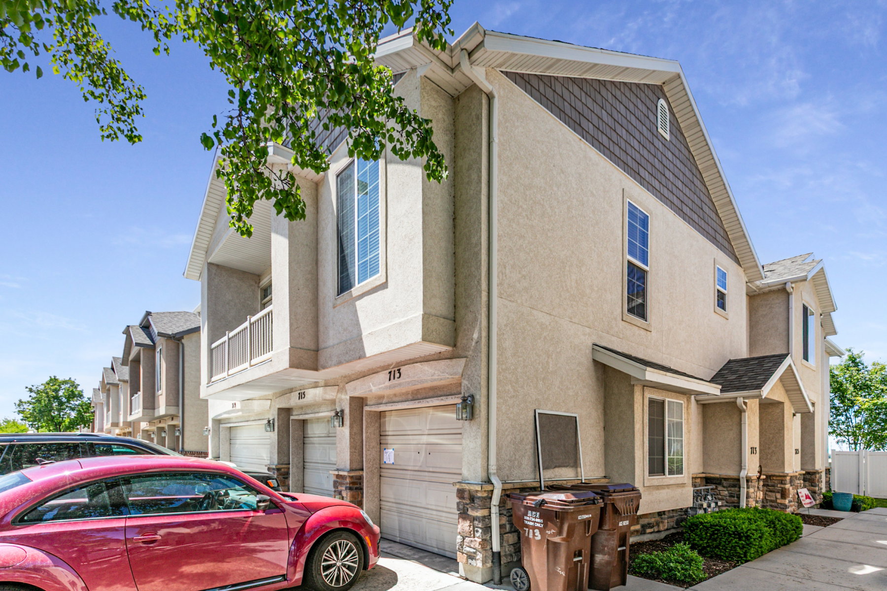 Contemporary townhome exterior featuring light-colored stucco siding, dark shake shingles on the gables, and stone veneer accents