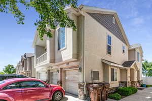 Contemporary townhome exterior featuring light-colored stucco siding, dark shake shingles on the gables, and stone veneer accents