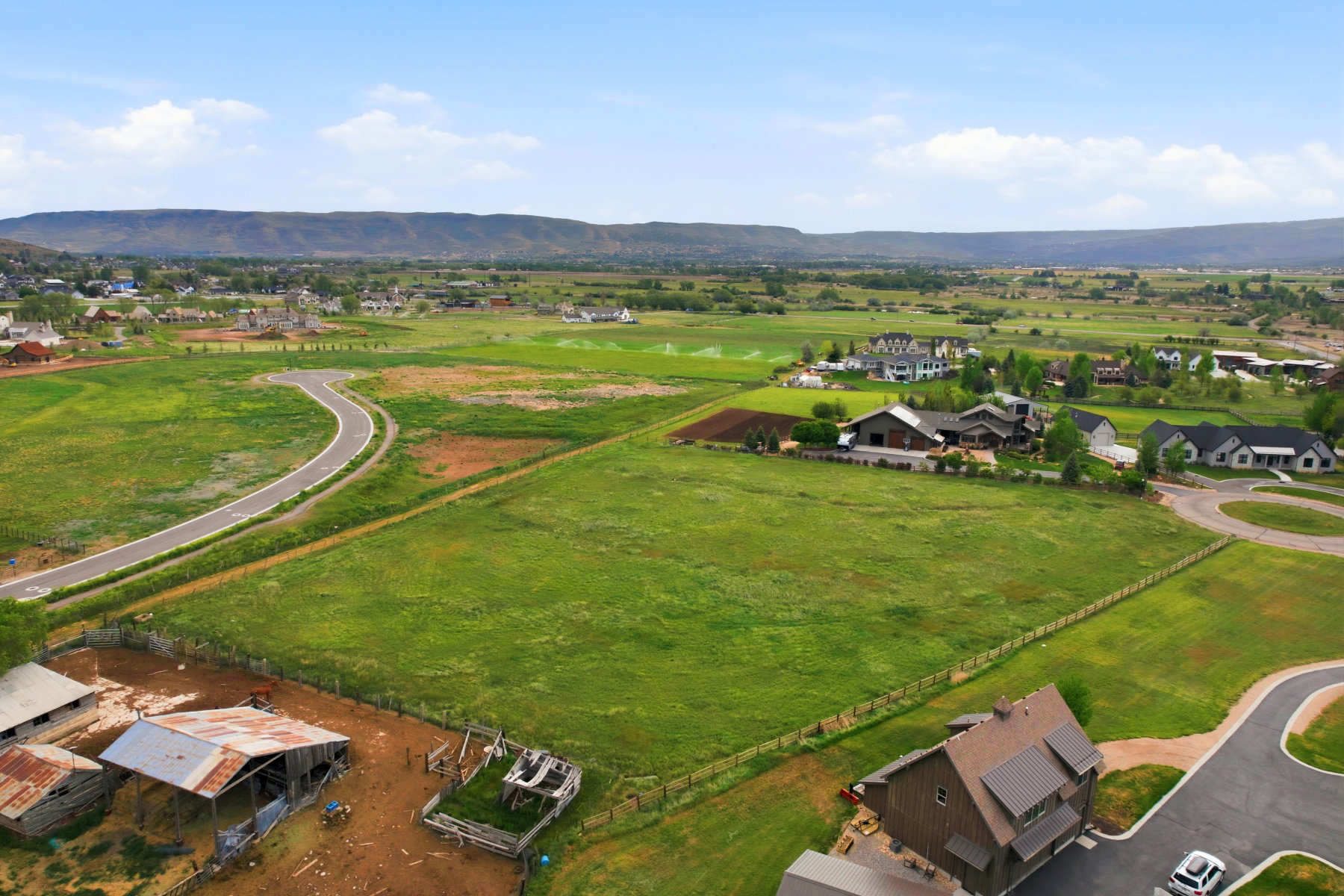 Expansive green fields with distant mountains and established residential structures