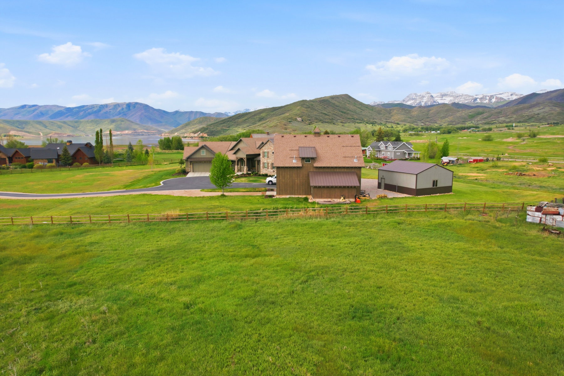 Expansive green landscape featuring a multi-level home with an attached garage, a separate barn-style structure, and an additional metal-sided outbuilding