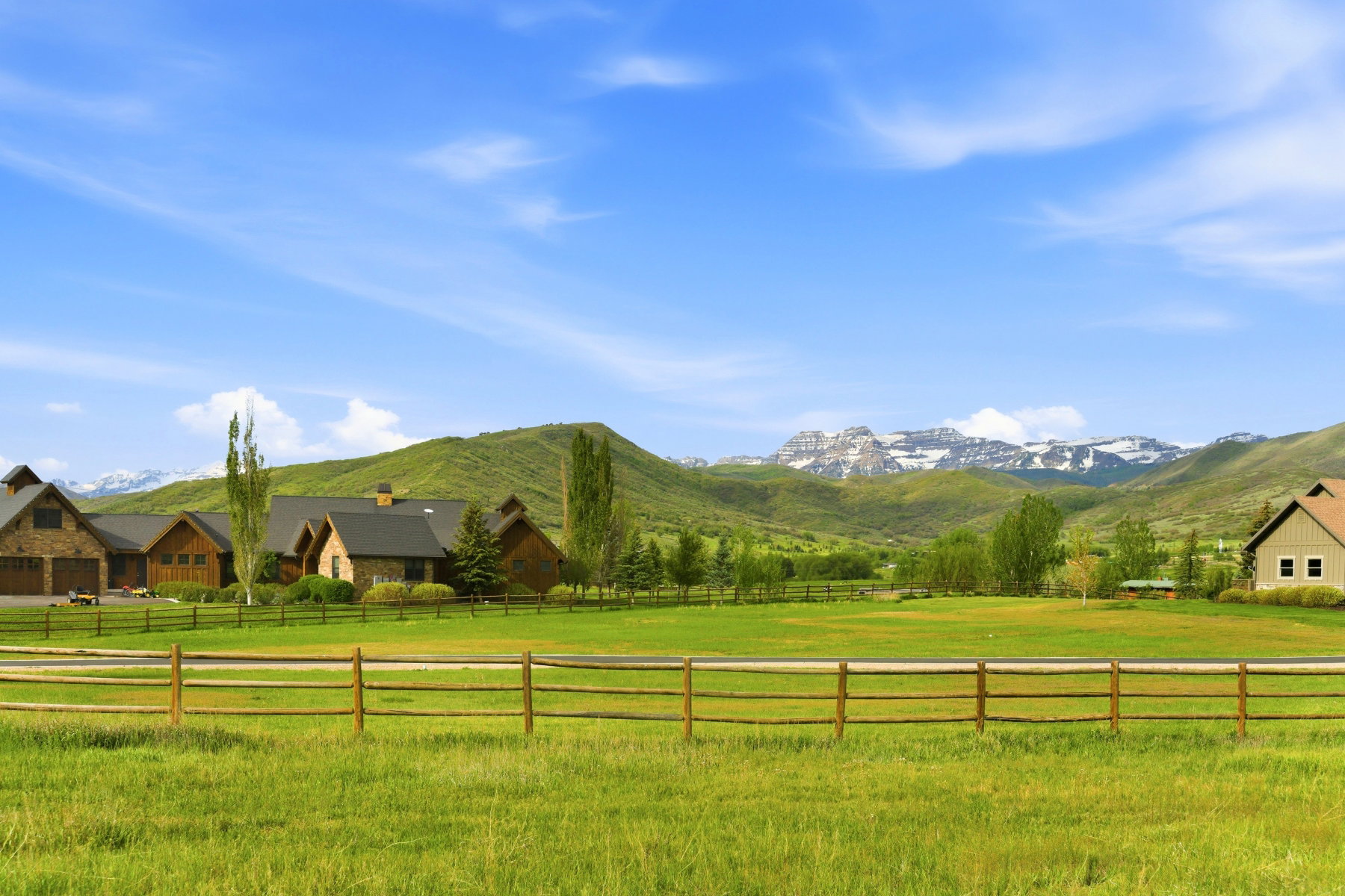 Expansive green acreage with a rustic split-rail fence, surrounded by rolling hills and distant snow-capped mountains
