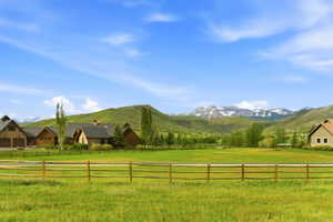 Expansive green acreage with a rustic split-rail fence, surrounded by rolling hills and distant snow-capped mountains