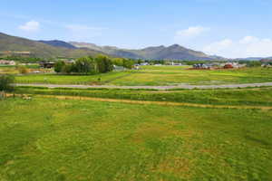 Expansive green fields extending towards distant mountains, featuring a paved roadway and scattered residential structures