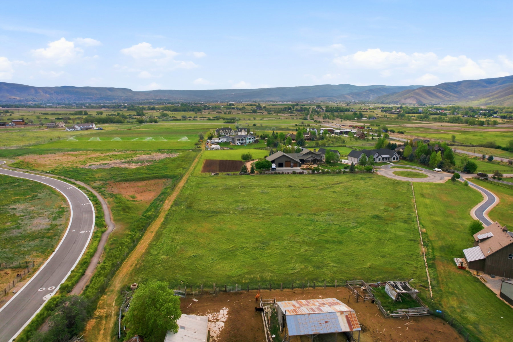 Expansive green acreage featuring a winding paved road and mountain backdrop