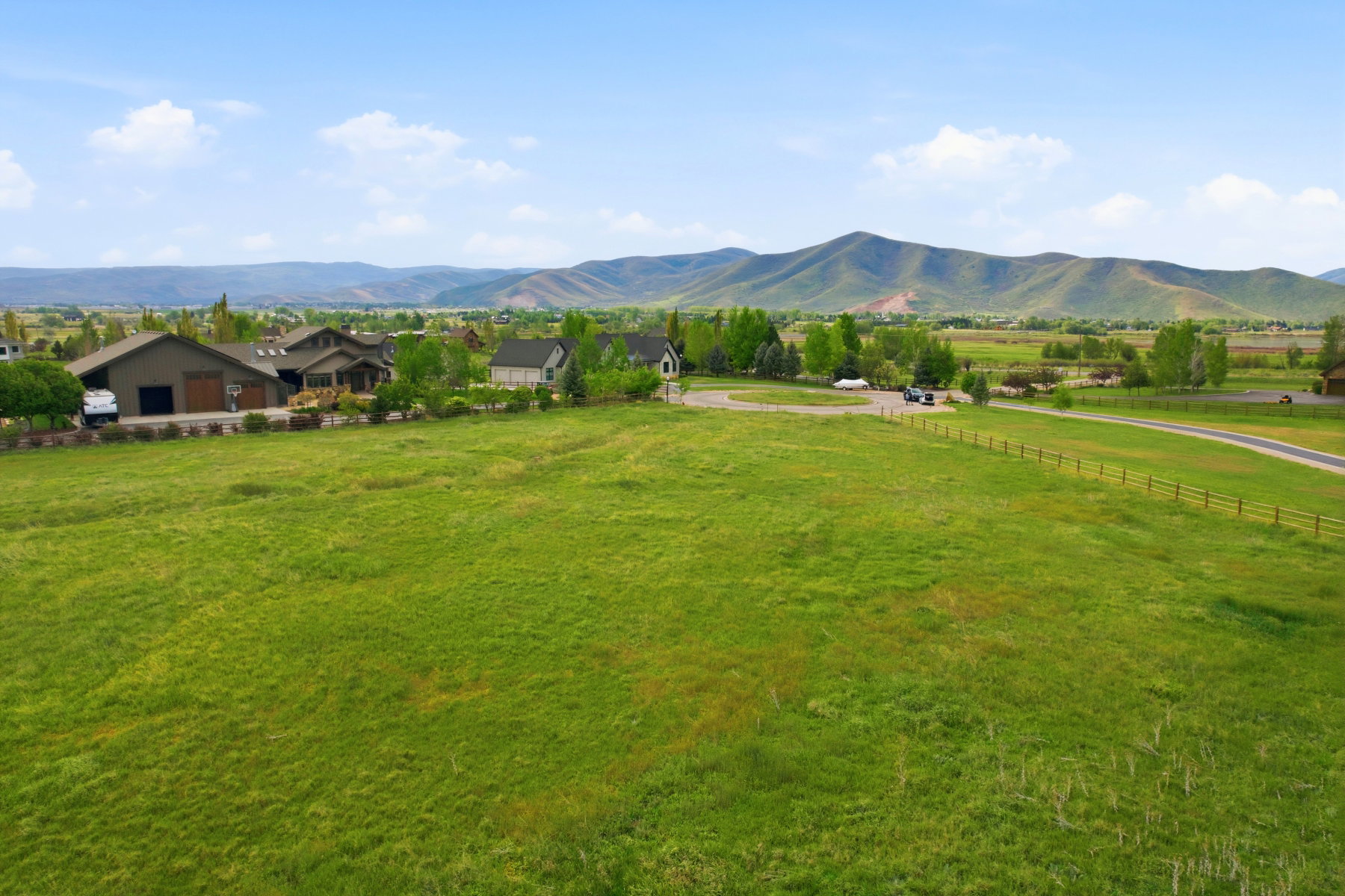 Expansive green pasture with a split-rail fence and a winding road