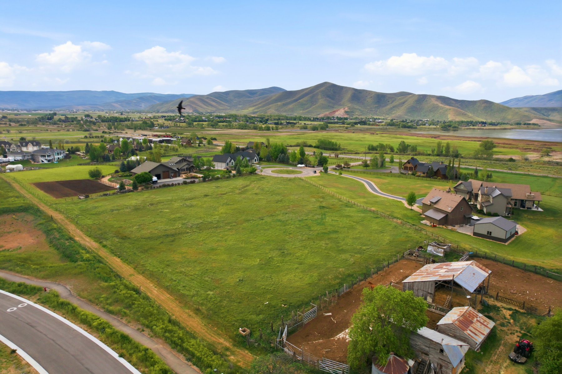 Expansive property featuring a large green field, surrounding residential structures, a visible body of water, and distant mountains