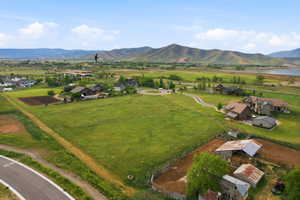 Expansive property featuring a large green field, surrounding residential structures, a visible body of water, and distant mountains