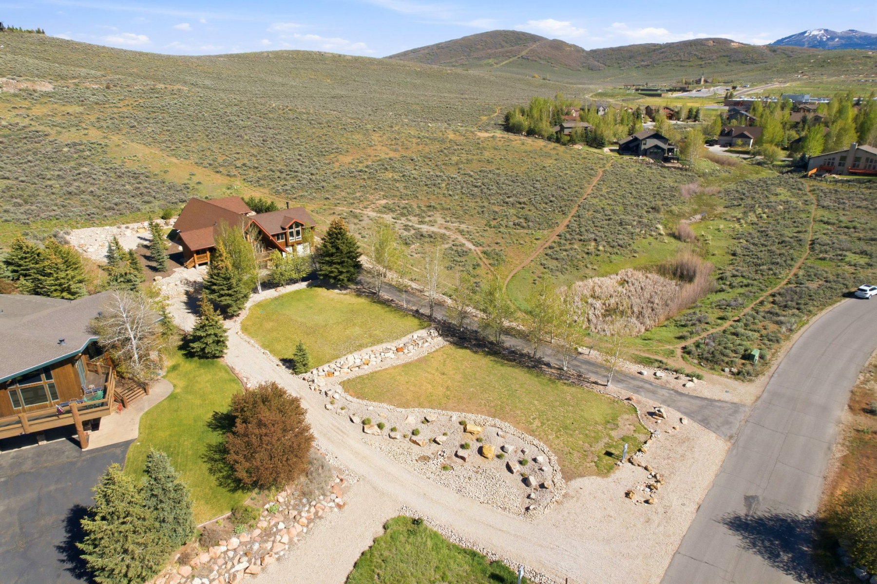 Expansive property featuring a brown multi-level residence with a distinct roofline, surrounded by established evergreen trees