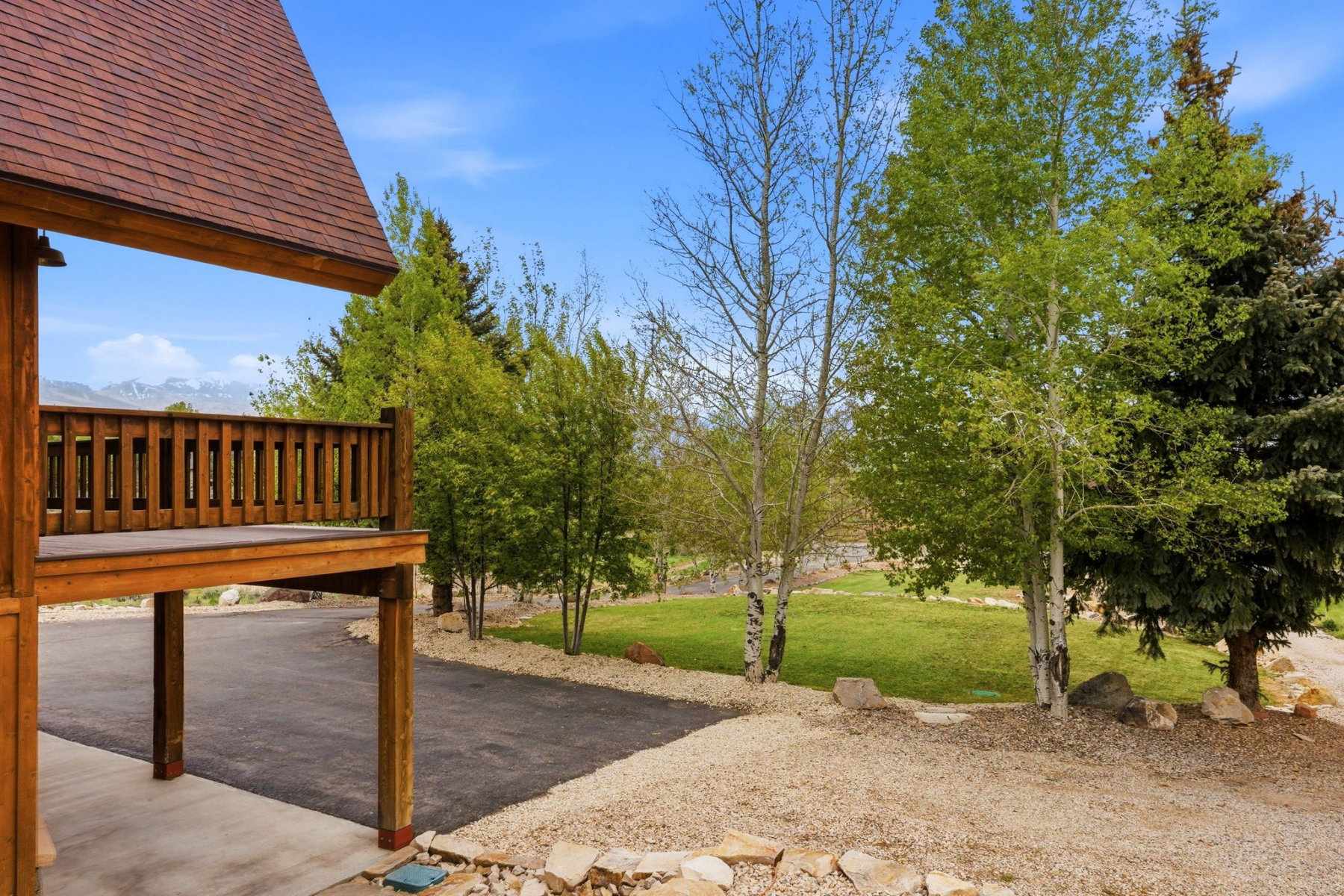 Raised wooden deck with a slatted railing, asphalt driveway, and a gravel landscape border