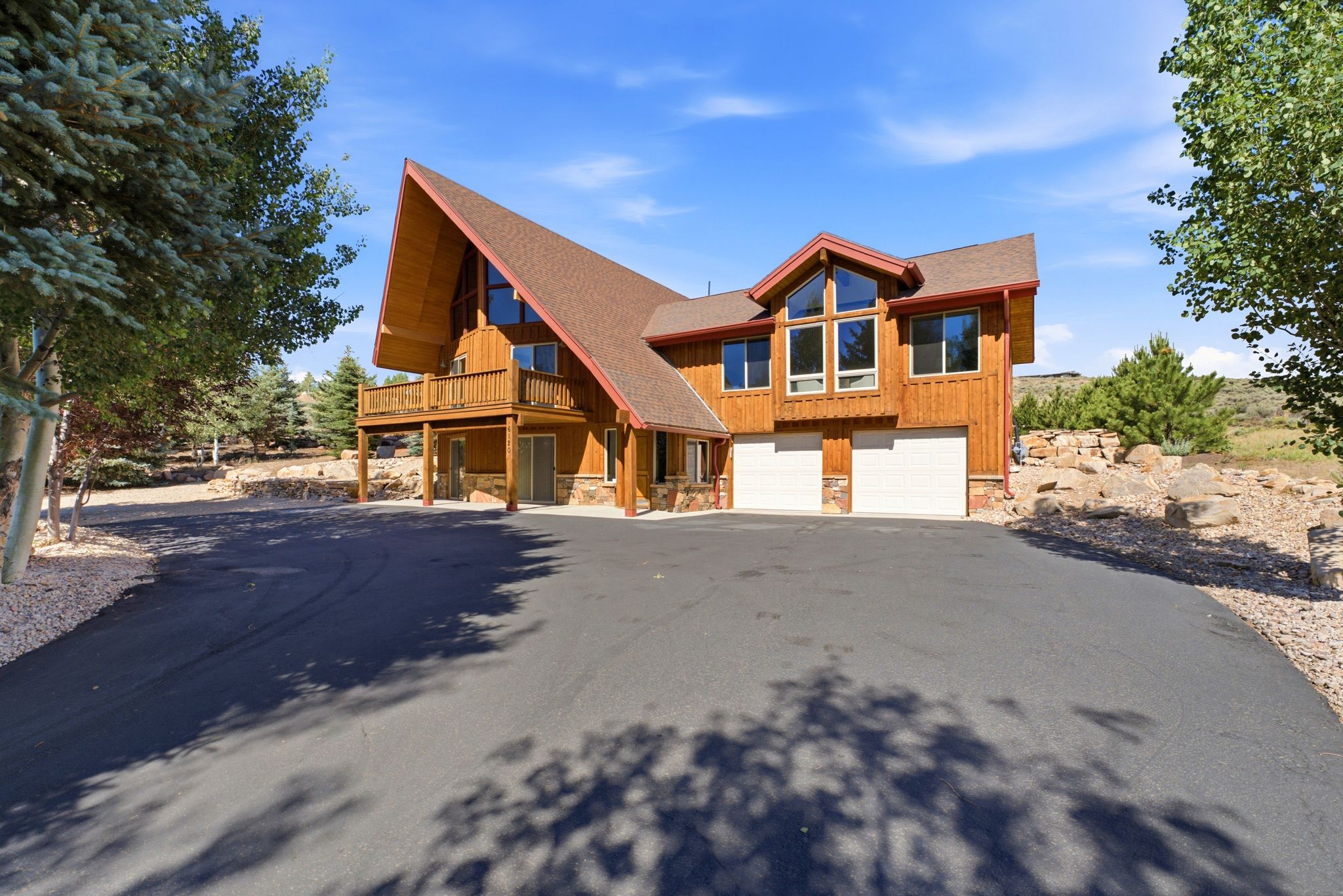 A-frame residence featuring natural wood siding, an asphalt driveway, multiple windows, a second-story balcony, and an attached two-car garage