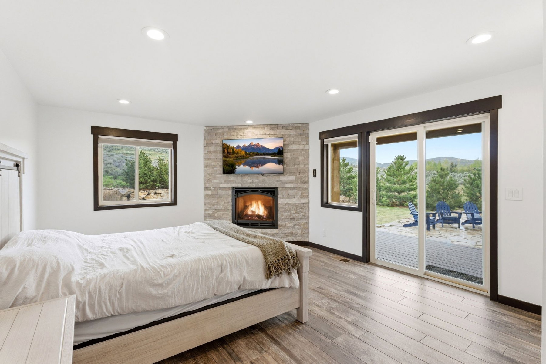 Spacious room featuring wood-finish flooring, a stacked stone fireplace, large windows, recessed lighting, and a sliding glass door to outdoor living