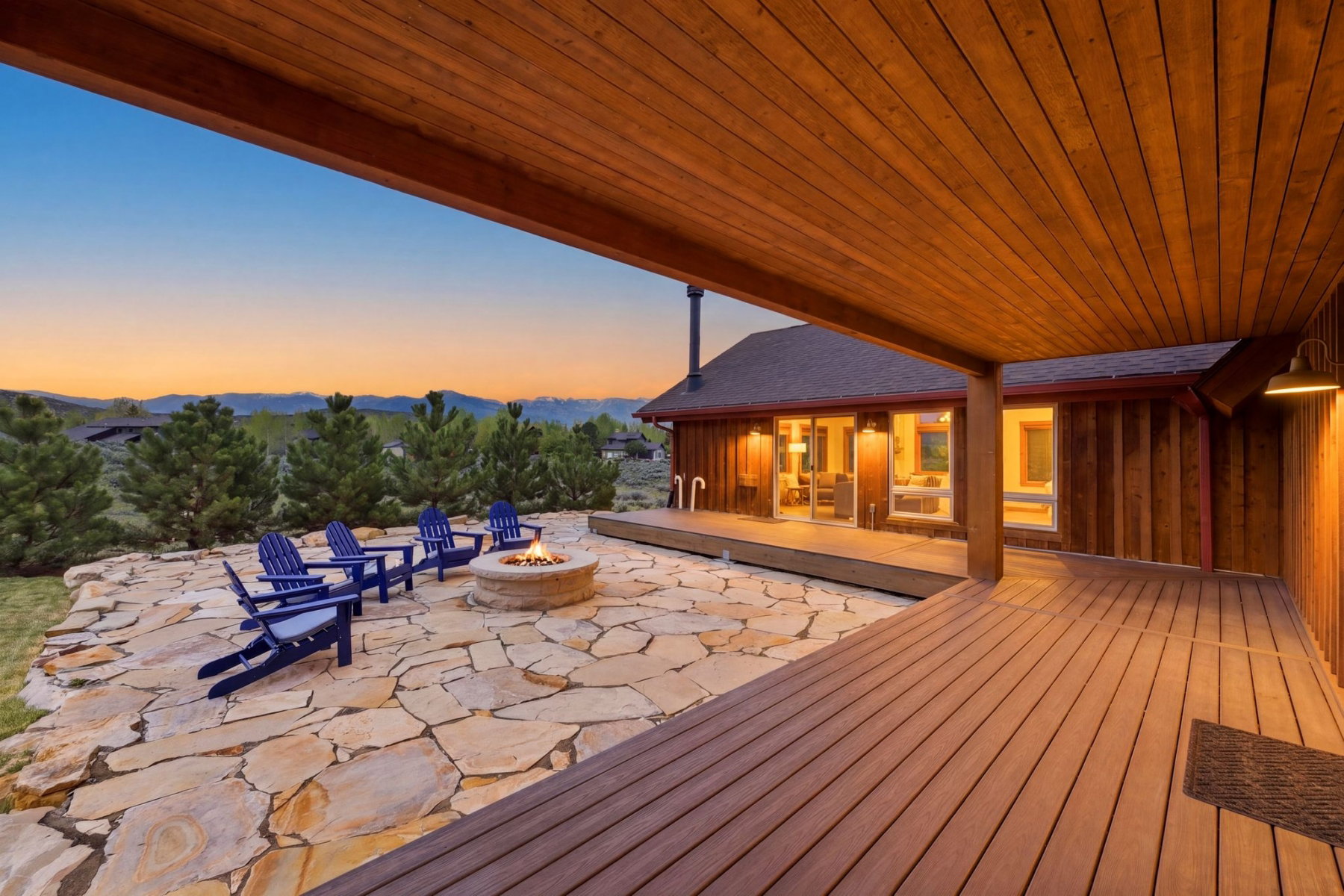 Expansive stone patio with a built-in fire pit, surrounded by mature evergreen landscaping