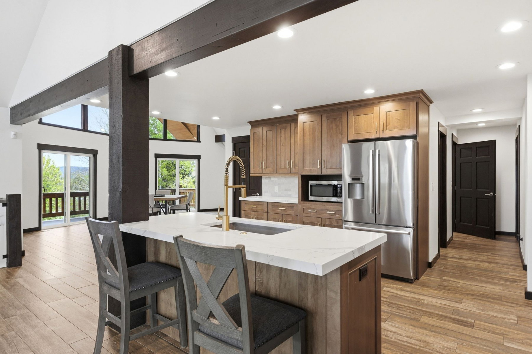 Open-concept kitchen featuring an island with a light-toned countertop, wood-finish cabinetry, stainless steel appliances, and recessed lighting