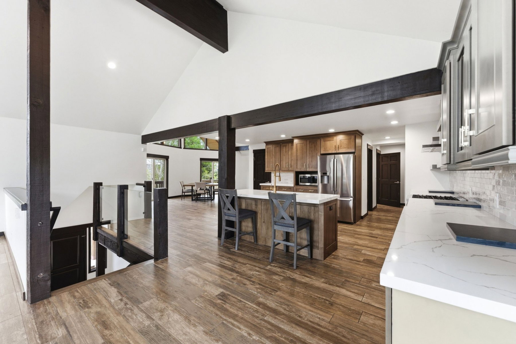 Open-concept kitchen and living area featuring vaulted ceilings, exposed dark wood beams, wood-finish flooring, a kitchen island with seating, and stainless steel appliances