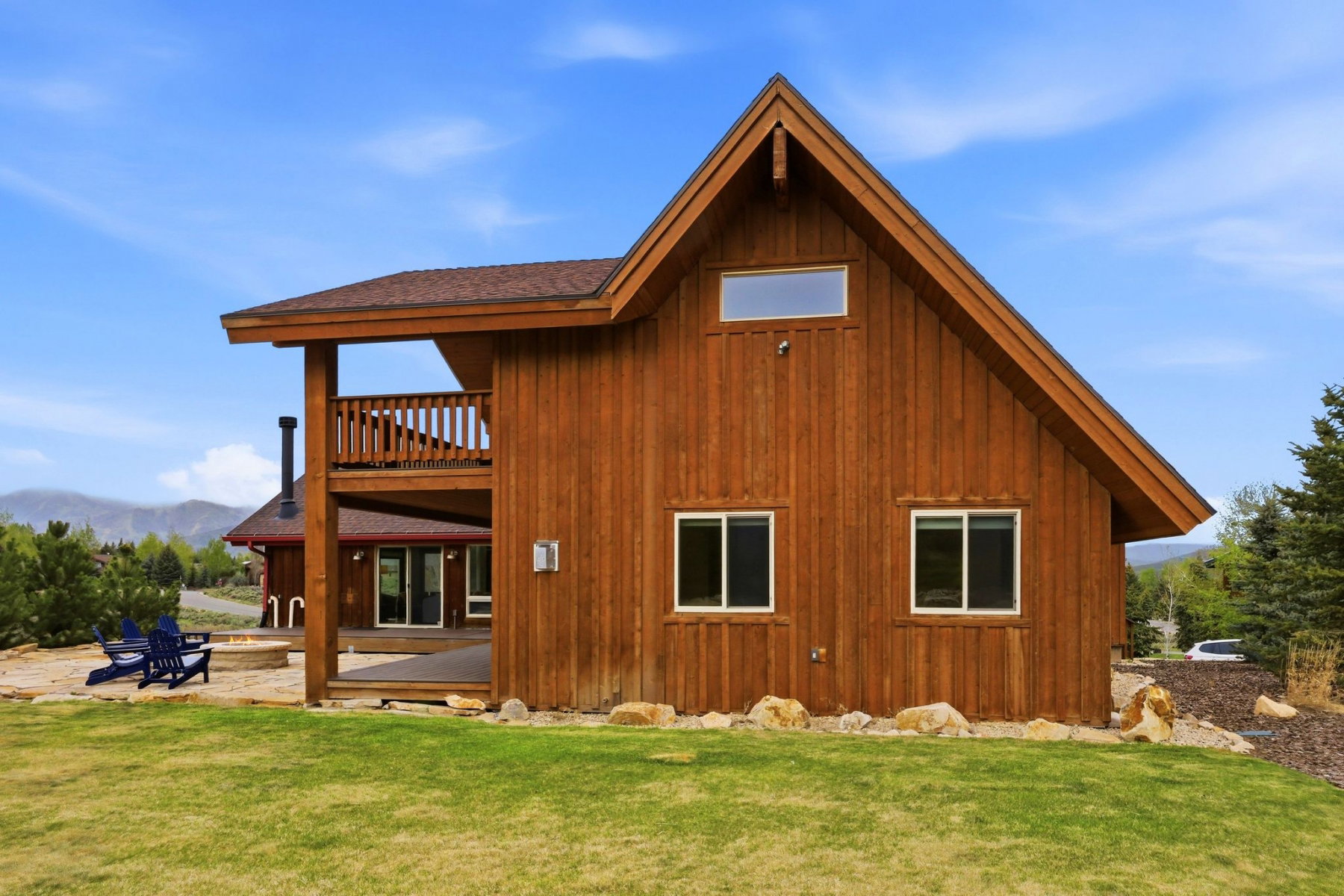 Wood-sided exterior featuring an A-frame gable, multiple windows, a second-story balcony with wood railing, and a ground-level patio