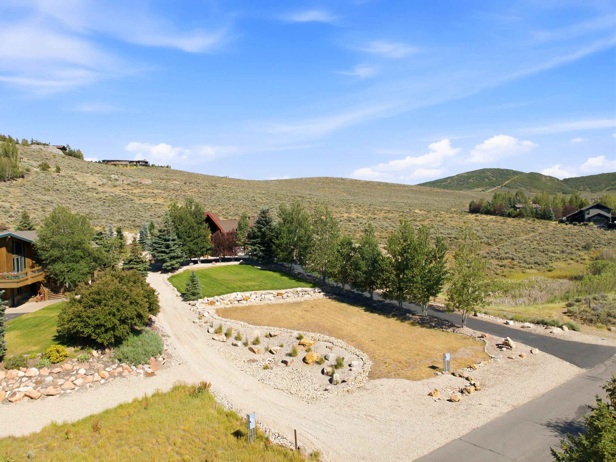 Expansive property featuring a gravel driveway, landscaped grounds with mature trees, and a manicured lawn area