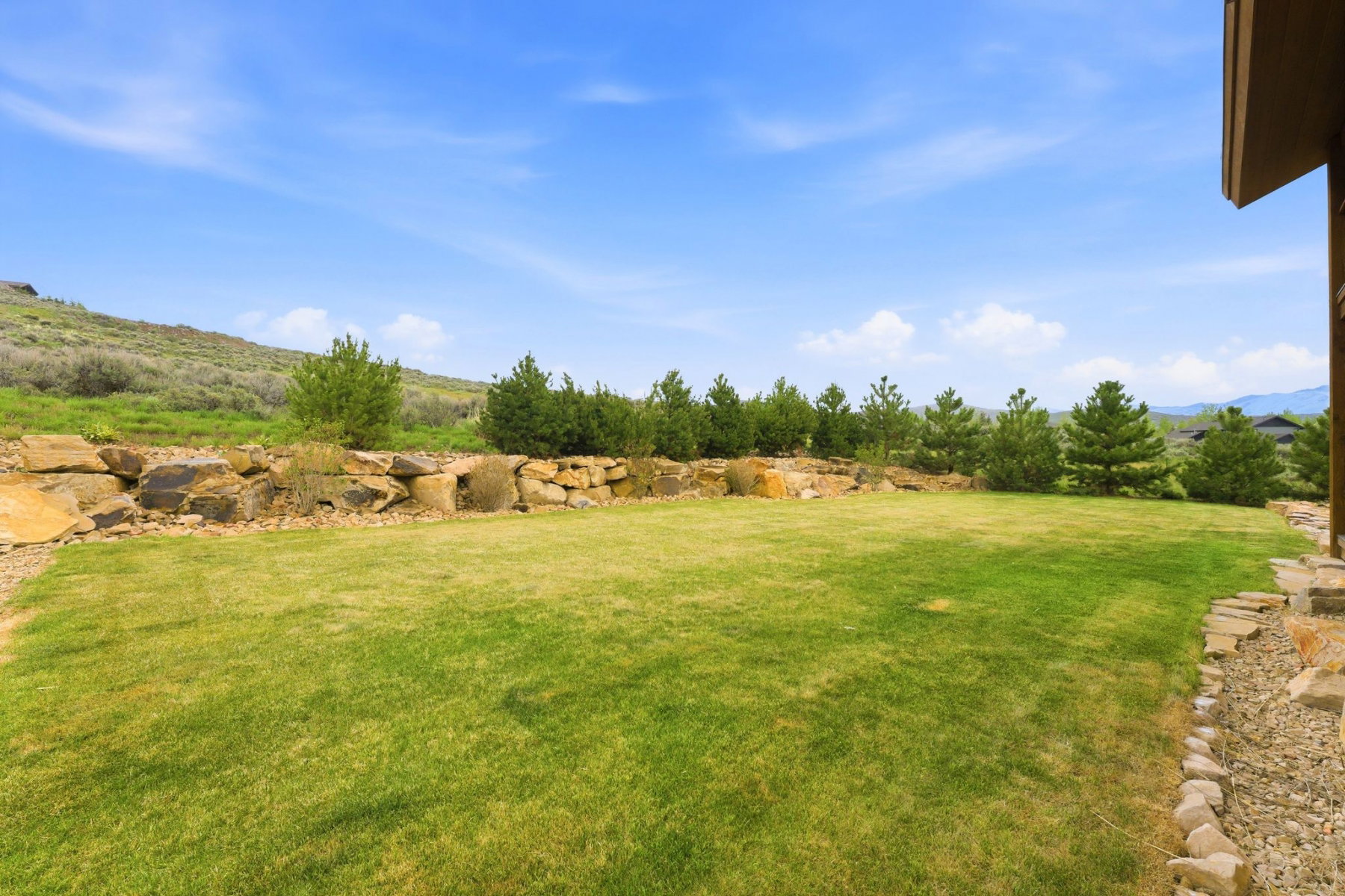 Expansive grassy lawn bordered by a natural stone retaining wall and mature evergreen trees