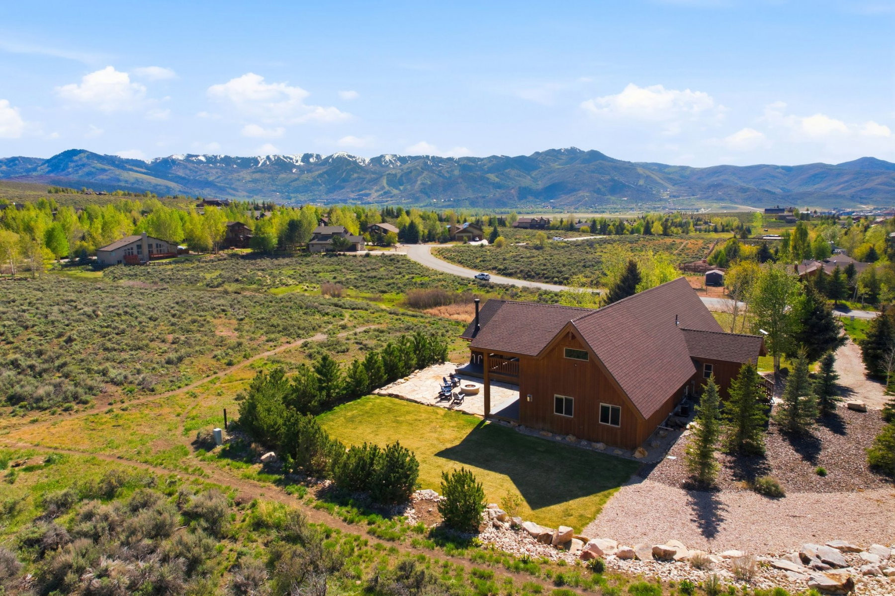 Wood-sided property with a brown shingle roof, featuring an outdoor patio, gravel driveway, and surrounding natural landscaping