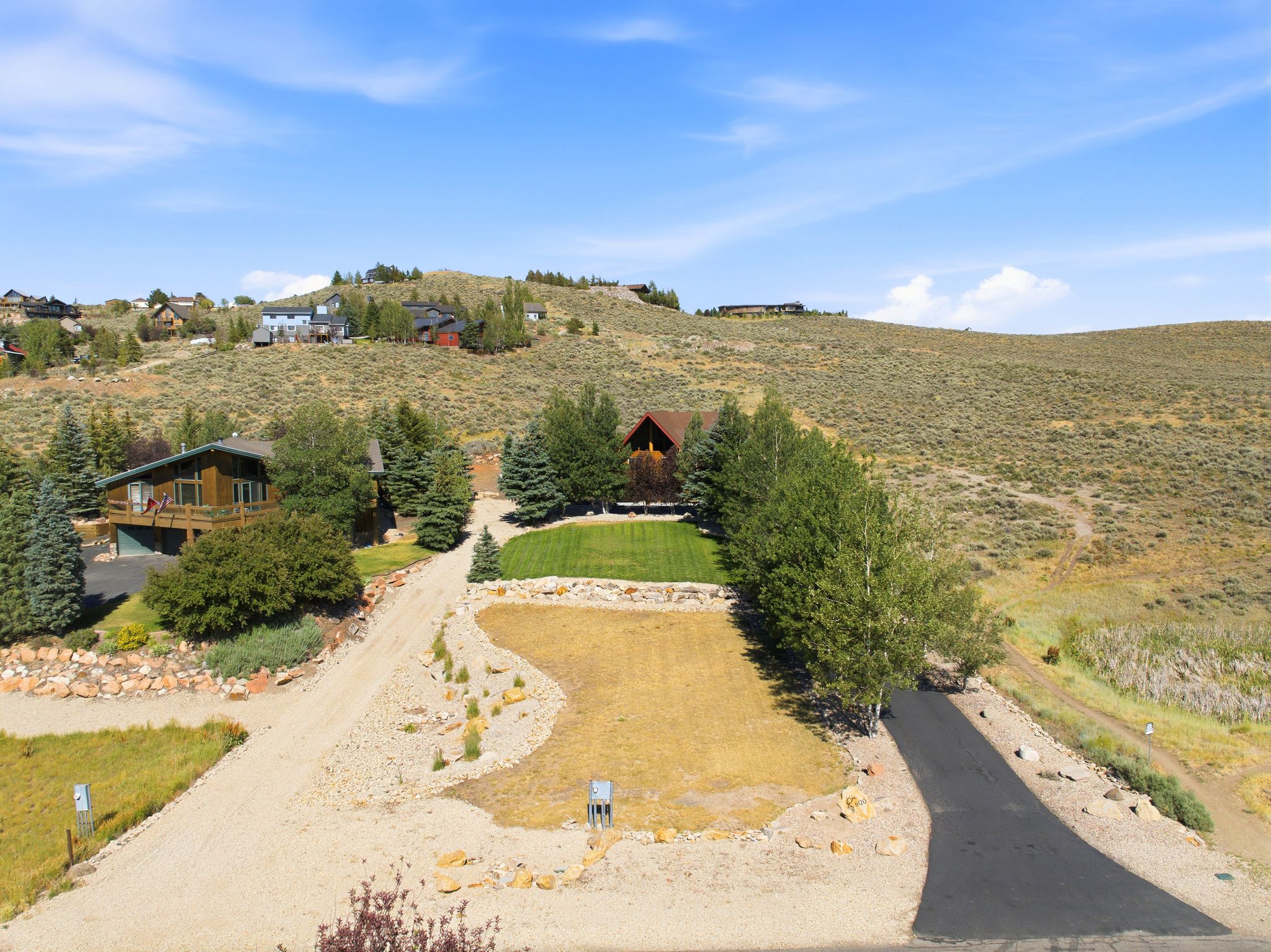 Expansive hillside property featuring a paved driveway, a gravel access road, and mature evergreen trees