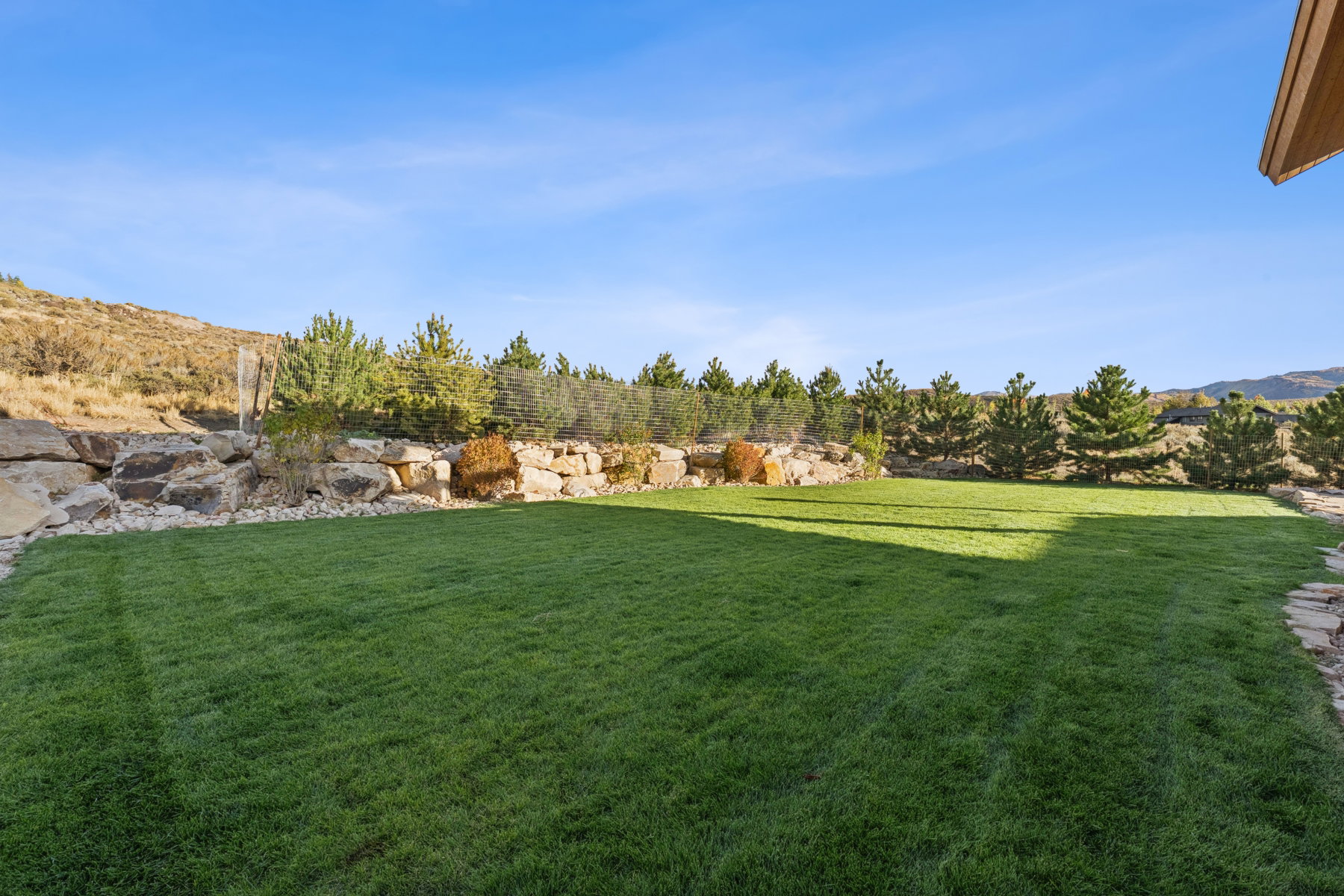 Expansive lawn area with a stone retaining wall and evergreen plantings