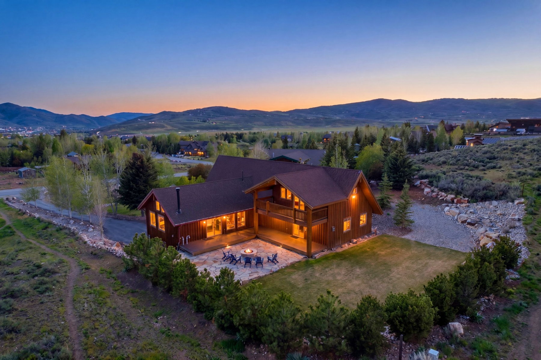 Log cabin architecture featuring an expansive stone patio, a turf lawn, and a second-story balcony